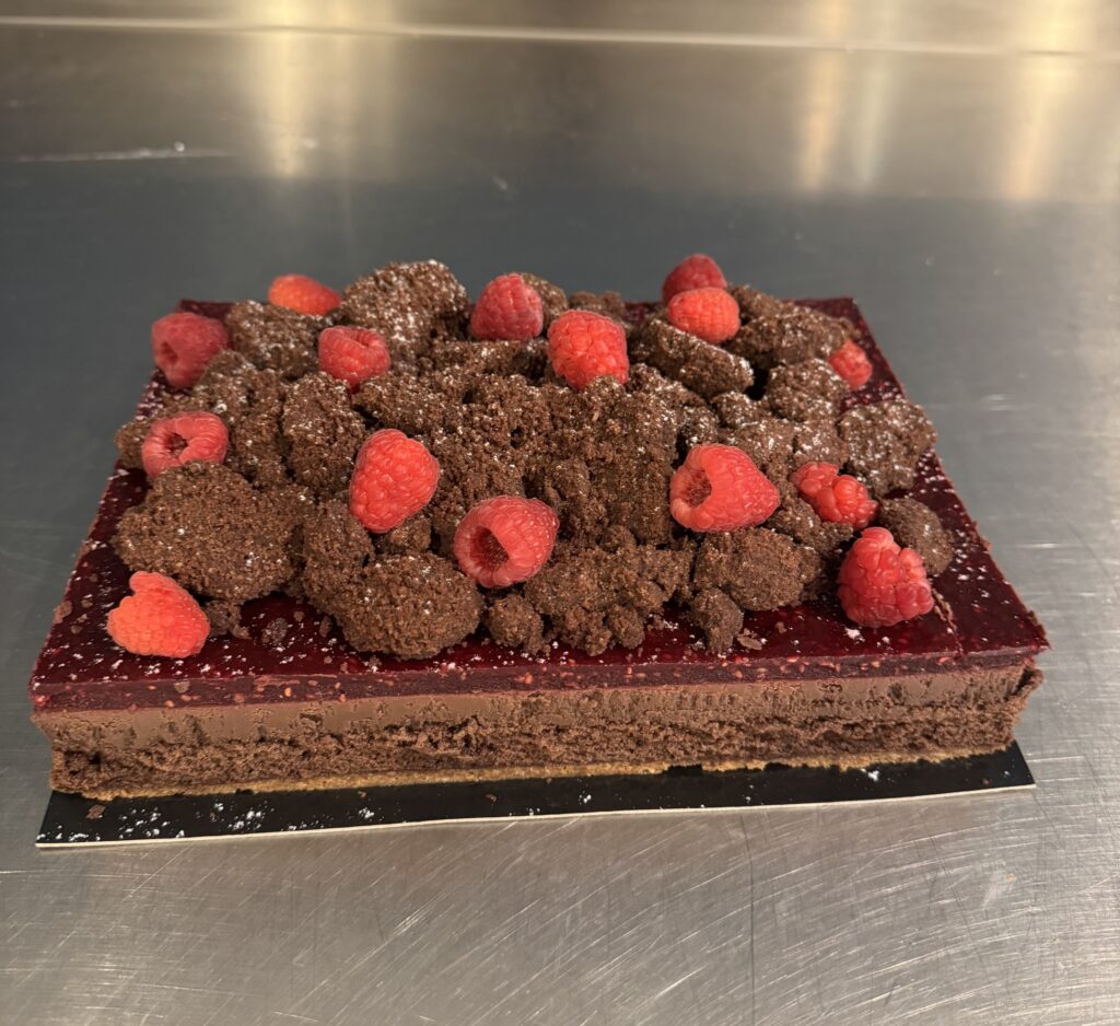 L’alliance intense du chocolat et de la framboise : croustillant praliné, biscuit chocolat, crémeux chocolat, compotée de framboises et streusel chocolat, sublimés par des framboises fraîches.
